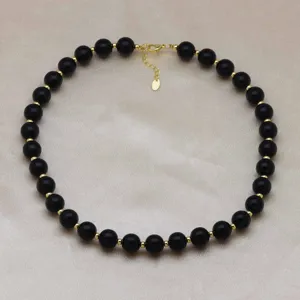 Collier de perles noires avec perles intercalaires dorées gros plan, accessoire bijouterie