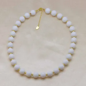 Vue détaillée d'un collier de perles blanches tendance avec des intercalaires métalliques dorés.