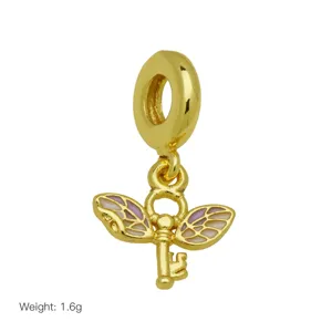Gold tone key dangle charm with enamel wings detail, close-up view of jewelry accessory.