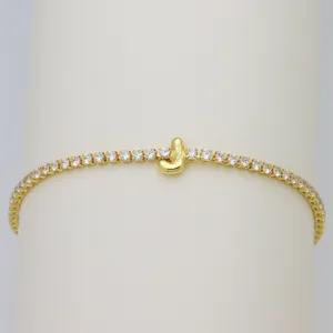 Closeup detail of gold tennis bracelet with cubic zirconia stones and cute letter charm jewelry.