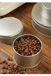 Detail view of round metal storage tin boxes filled with fresh coffee beans on wooden table.