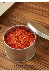 Round metal tin box detail featuring smooth metallic texture and red dried flower filling inside.