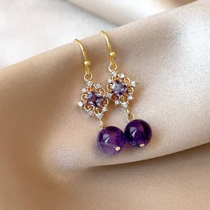 Boucles d'oreilles pendantes en pierre violette avec filigrane d'or et strass brillants.