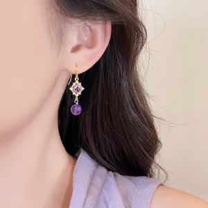 Gros plan détaillé de la boucle d'oreille en cristal violet au design filigrane doré.