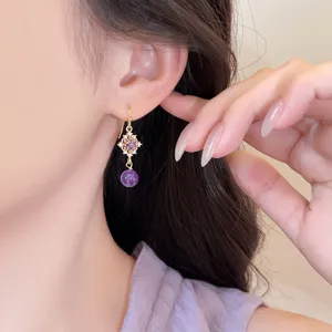 Gros plan d'une boucle d'oreille losange élégante avec pierre violette et aiguille en argent.