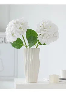 Close-up detail of artificial white hydrangea flowers in a ceramic vase for home decor setup.