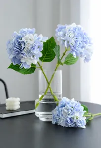 Artificial hydrangea flowers in clear glass vase, elegant blue faux floral decor for home wedding.