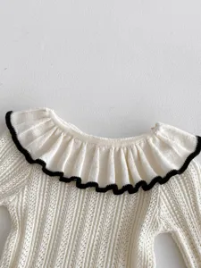Detailansicht eines weißen Baby-Stricktops mit süßem, schwarz eingefasstem Rüschenkragen.