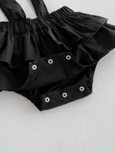 Detaillierte Nahaufnahme des schwarzen Babystramplers mit Rüschen und Druckknöpfen Textur