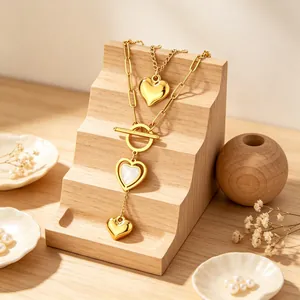 Detalle de collar dorado multicapa con colgantes de corazón e incrustación de nácar.