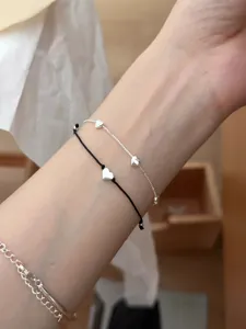 Primer plano detallado de la fina cadena de plata y la pulsera de cordón con corazón.