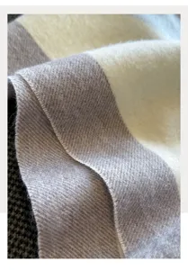 Close-up detail of soft woolen plaid scarf texture, showing fine herringbone and warm fabric.