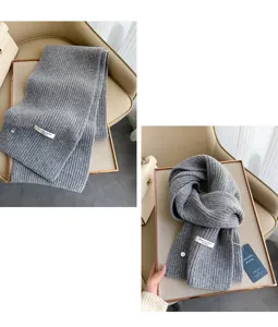 Grauer Wollstrickschal Detail zeigt weiche Textur und Markenetikett, warmes Winteraccessoire.
