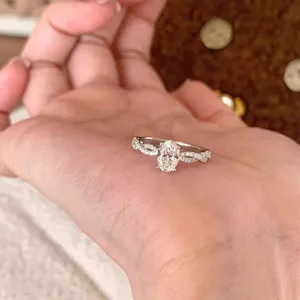 Primer plano del delicado anillo pavé trenzado con detalle de piedra central ovalada.