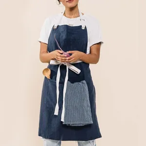 Close-up of dark blue linen apron with practical pockets holding wooden spoon and striped cloth.