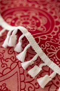 Detail nappe jacquard rouge avec franges blanches delicates et motif floral dore traditionnel.