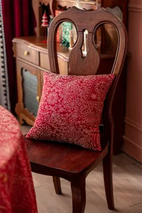 Vue détaillée du coussin décoratif rouge avec motif cachemire doré sur chaise en bois.