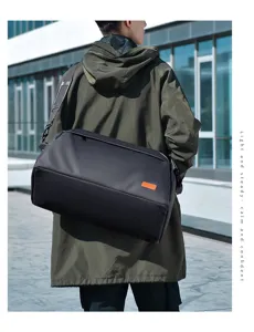 Detail shot of large capacity black travel duffel bag with orange tag worn outdoors.