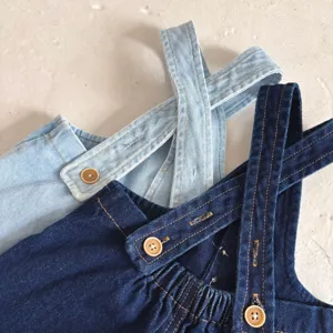 Dettaglio salopette di jeans per neonati, cotone morbido, spalline incrociate e bottoni.