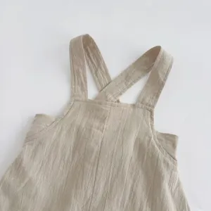 Baby linen romper cross strap detail, natural beige color, soft fabric texture close-up.
