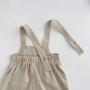 Baby linen romper detail shot showing adjustable crossed shoulder straps and cute buttons.