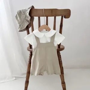 Baby summer clothing set detail, white blouse and beige overall shorts with sun hat.