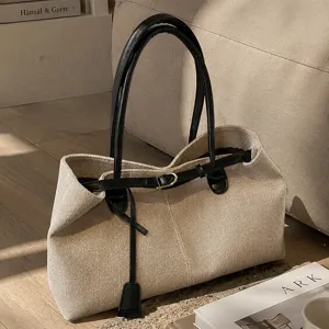 Detailed view of beige canvas tote bag with black leather handles and stylish belt strap accent.