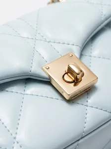 Gros plan sur les détails du sac en cuir matelassé bleu clair avec fermoir tournant doré.