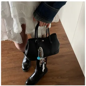 Detailed view of the black leather handbag, showing texture, turn-lock and chic charm accessory.