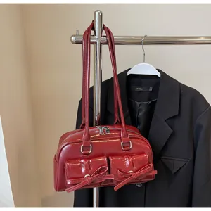 Détail de sac à bandoulière rouge vernis avec doubles anses et poches à nœuds.