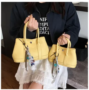 Detail view of stylish yellow leather handbag with dual top handles and cute charms.