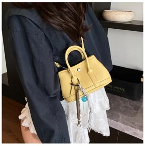 Detail view of stylish yellow mini handbag featuring top handles, crossbody strap and cute charms.