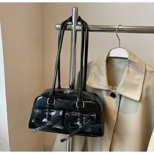 Détail en gros plan du sac porté épaule en cuir vernis noir avec poches à nœud.