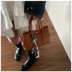 Brown leather tote handbag with top handles and stylish bag charms, perfect for daily commuting.