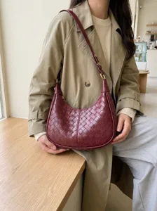 Detail shot of a dark red woven leather shoulder bag worn by model in a cozy cafe setting.