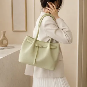 Close-up of light green woven tote bag with belt buckle detail carried by model.