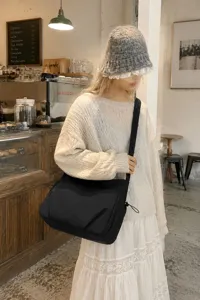 Detailed lifestyle view of a casual black nylon crossbody shoulder bag in a cozy cafe setting.