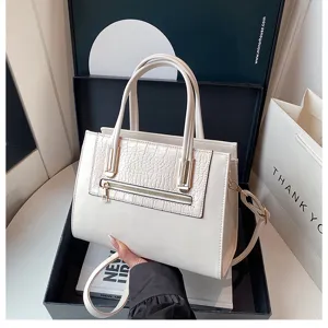 Detail view of white handbag with crocodile texture panel, gold-tone zipper, and dual top handles.