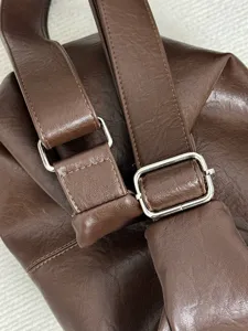 Close-up detail of the brown soft leather bag strap with silver metal buckle and stitching.