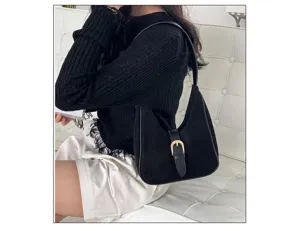 Close-up detail of a black suede hobo shoulder bag with a gold buckle strap worn by model.