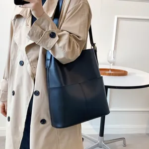 Minimalist black leather bucket bag detail, casual shoulder crossbody wear in interior setting.