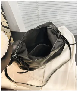 Detalle del bolso de hombro de cuero negro con interior espacioso y bolsillo con cremallera.