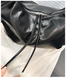 Primer plano detallado de bolso de hombro en piel negra con cremallera y tiras largas.