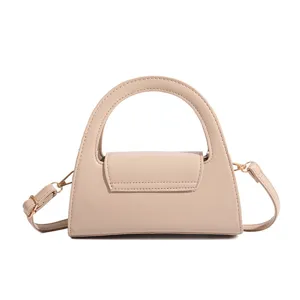 Detail view of beige trapezoid handbag with arch handle and metal hardware elements.