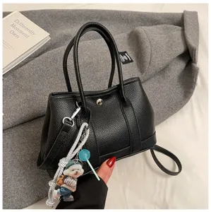 Detailed view of a stylish black leather handbag with cute dog charm and top handles.