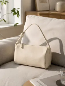 Minimalist cream cylindrical shoulder bag detail, textured leather barrel shape design.