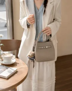 Vue détaillée du sac à main élégant en cuir gris avec fermoir en métal et charm d'ourson en peluche.