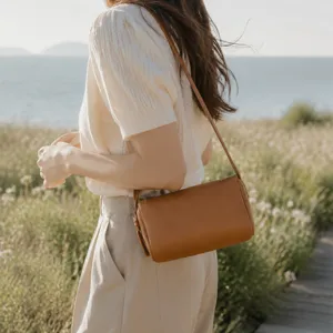 Outdoor detail view of minimalist brown leather cylinder crossbody bag with fine texture.