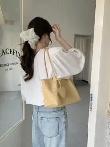 Detail view of stylish yellow woven shoulder tote bag with heart charm, casual daily commute style.