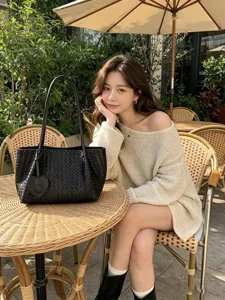Detailed shot of a black woven shoulder tote bag with heart charm, styled in a cafe setting.